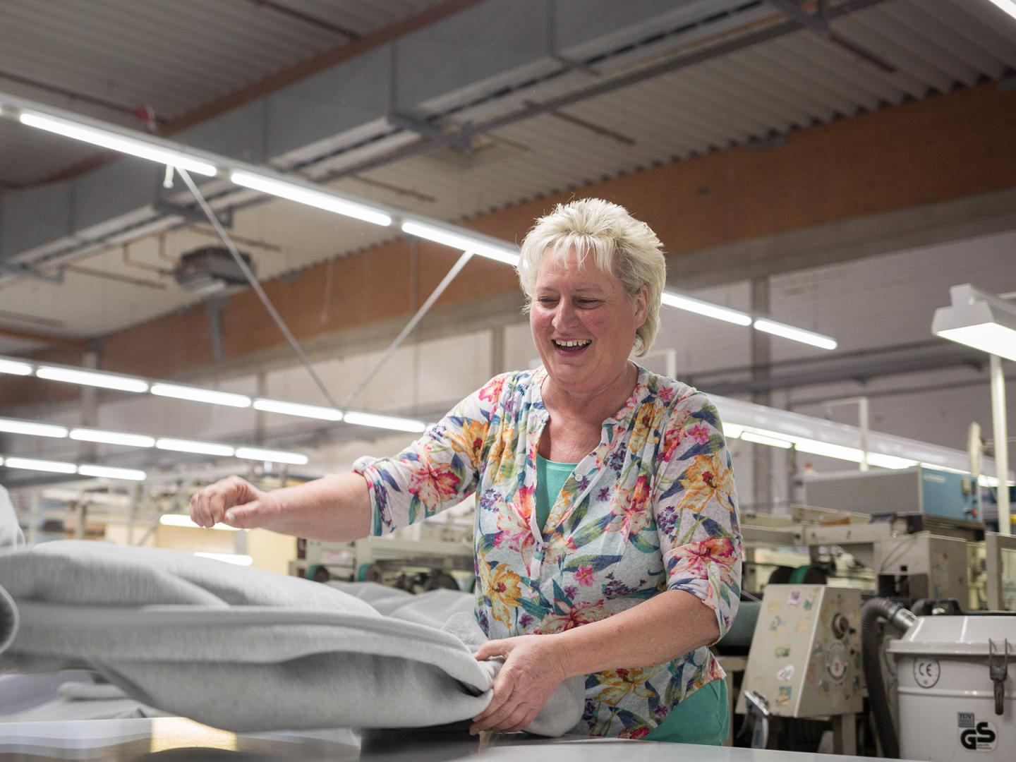 Eine Frau mit Blonden kurzen Haaren wirft lachend eine Stoffbahn aus.
