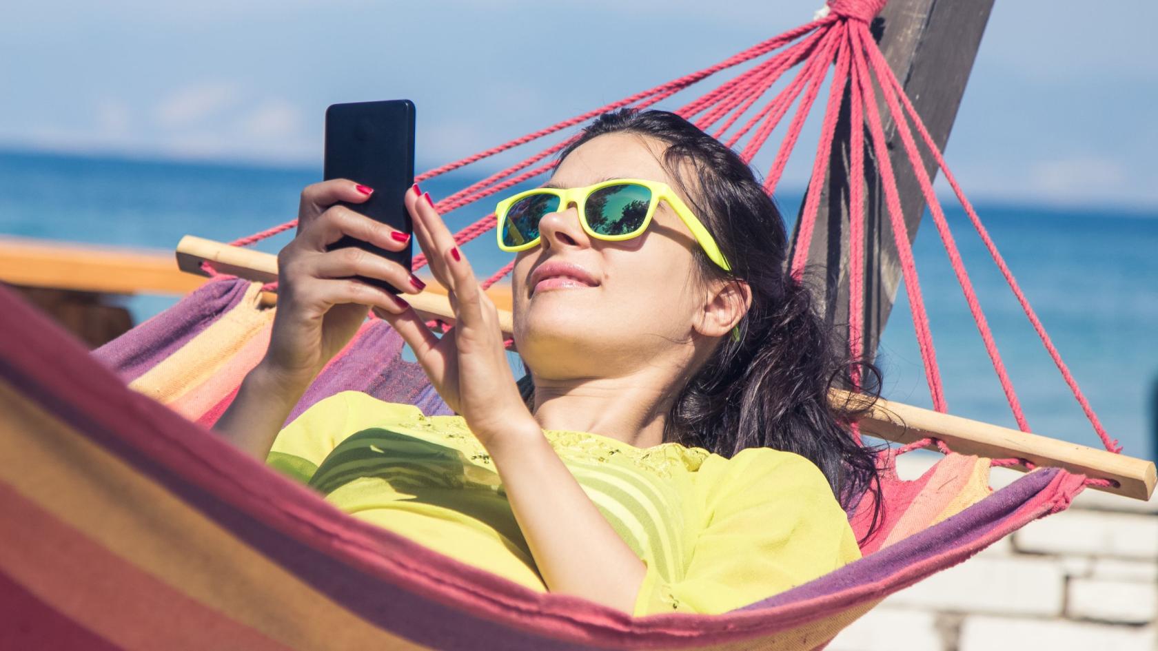 Junge Frau liegt mit ihrem Smartphone in einer Hängematte