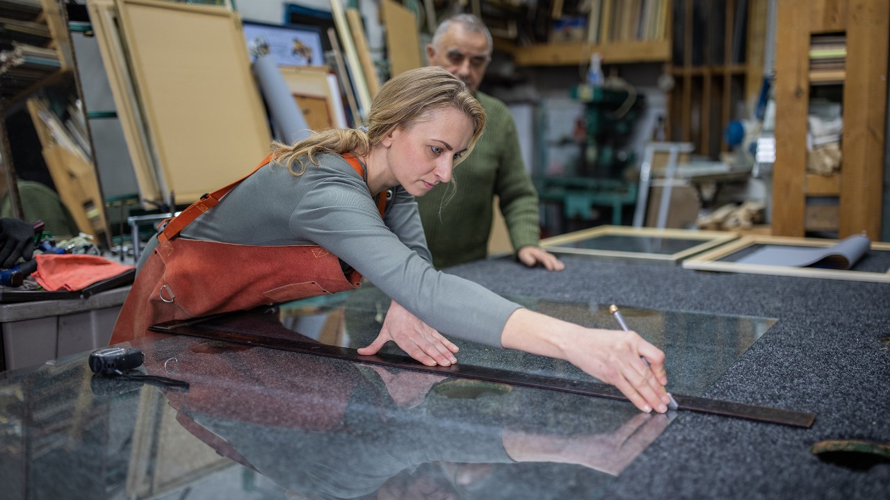 Eine Glaserin schneidet in der Werkstatt Glas zu