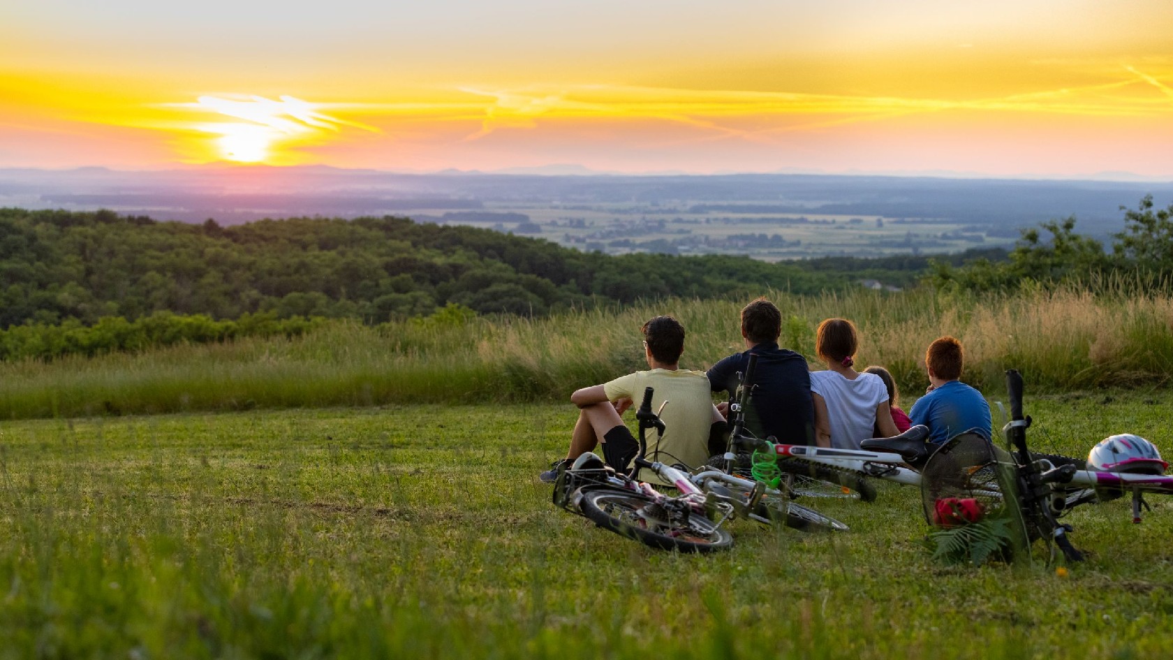 Familie, die nach einer Radtour auf einem Hügel sitzt und den Sonnenuntergang betrachtet 